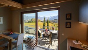 A dining area with a table and chairs, a wine rack, and a view of a vineyard through large sliding doors. - The key to more freedom (Eppan an der Weinstrasse)
