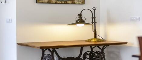 A corner room with a wooden table, a vintage-style lamp, and a decorative mirror on the wall.