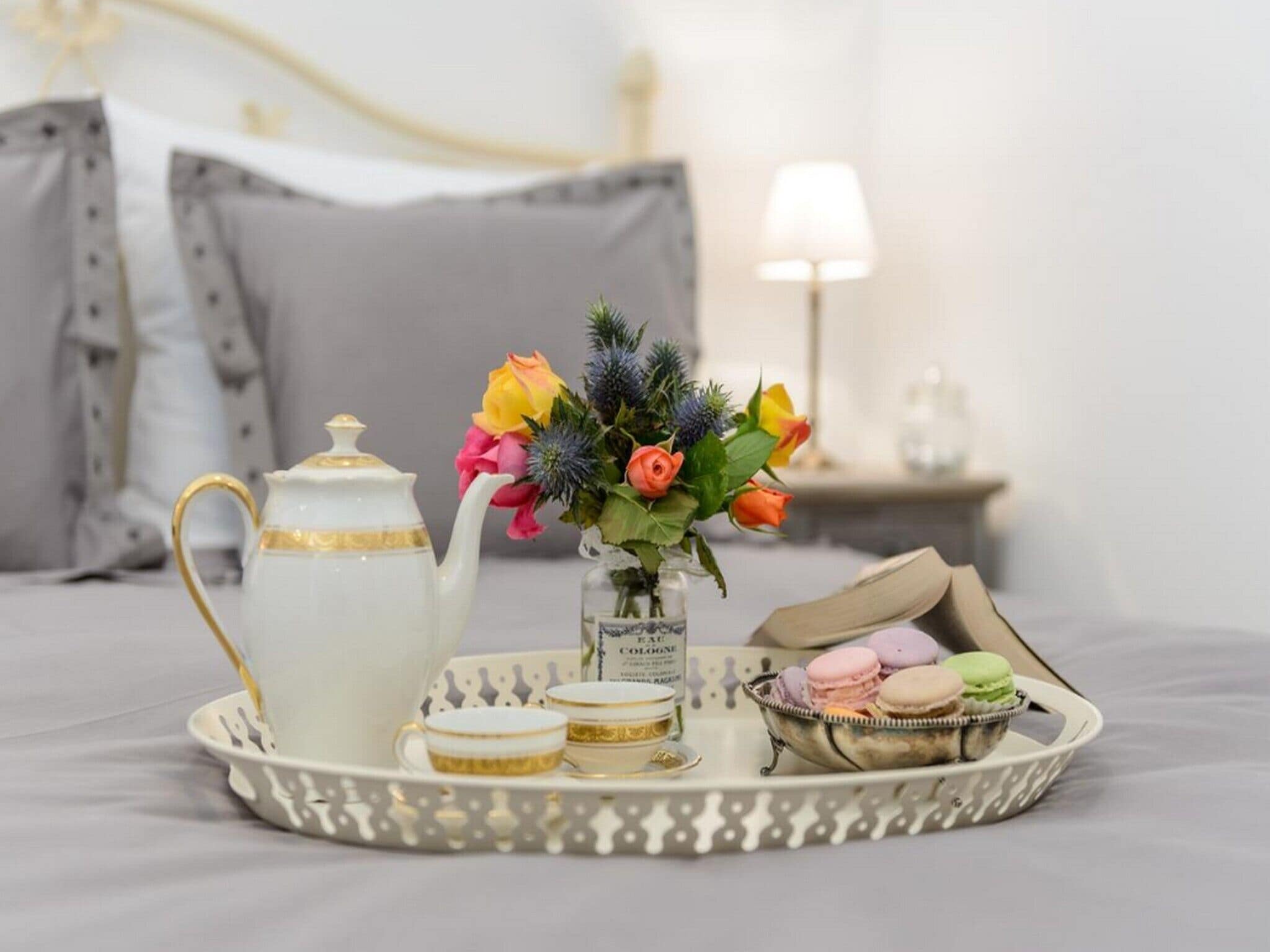 A tray with a teapot, cups, a vase with flowers, and macarons on a bed.