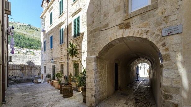 A stone building with an arched passageway, potted plants, and a sign indicating a direction to the city walls. - Apartments Franka Old Town (Dubrovnik)