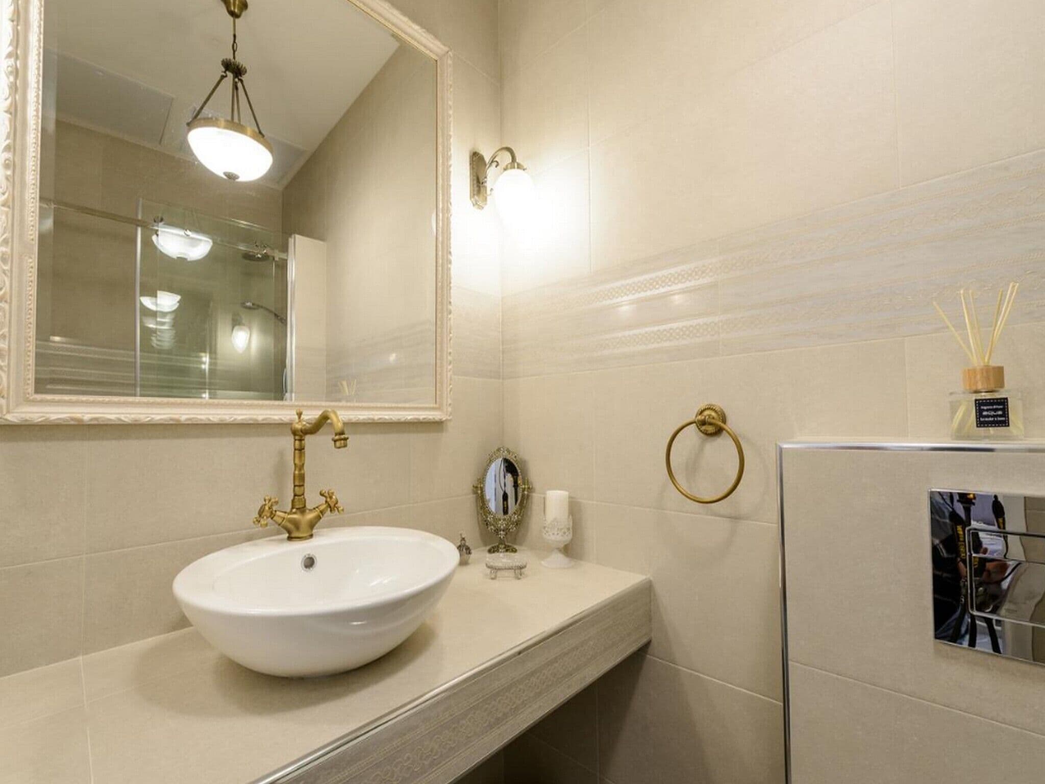 A bathroom with a white sink, gold faucets, a mirror, and a towel ring.