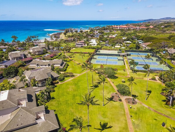 An aerial view of a residential area with houses, a tennis court, and a view of the ocean.