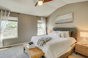 Een slaapkamer met een groot bed, een bedlampje, een raam met gordijnen en een plafondventilator.