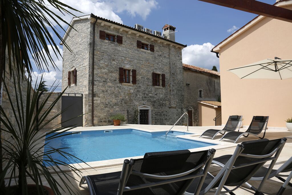 A stone building with a swimming pool and lounge chairs.