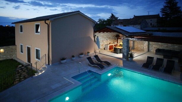 Una piscina con sillas de descanso, un edificio de piedra y un espacio exterior cubierto.