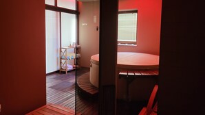 Un baño moderno con una banca de madera, un separador de vidrio y un techo iluminado en rojo.