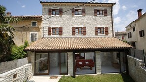 Un edificio de piedra con tejado de tejas, ventanas grandes con contraventanas y un porche cubierto.