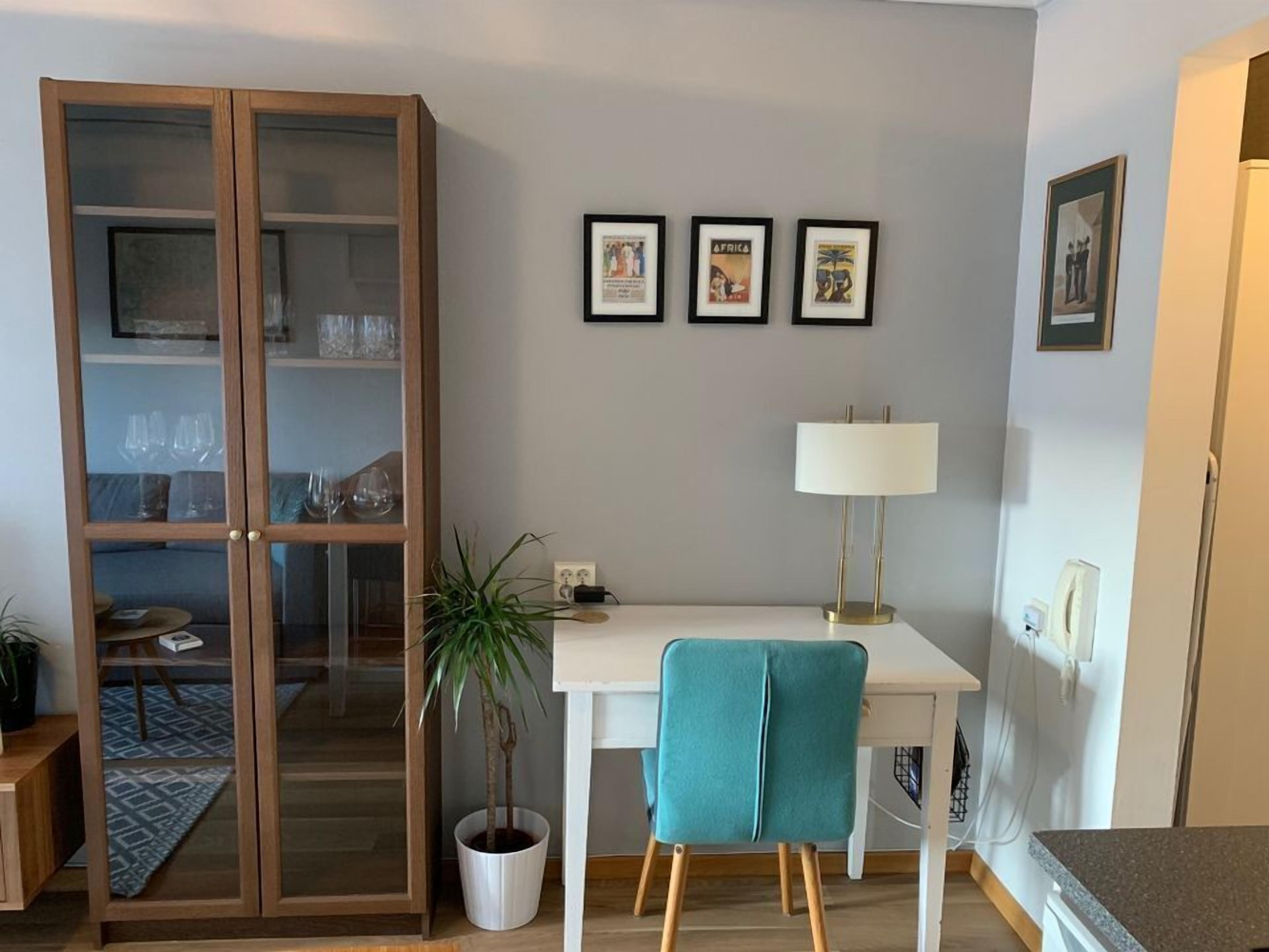 Un salon moderne avec un meuble vitré, un bureau blanc, des chaises de couleur turquoise et une plante en pot.