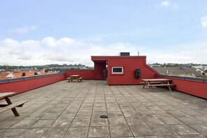 A rooftop terrace with red walls, picnic tables, and a small enclosed area with a window.