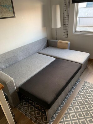 A compact living space with a grey sofa, a small wooden side table, a floor lamp, and a patterned rug.