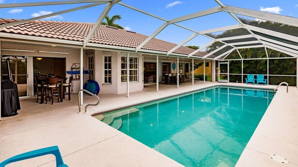 Une piscine couverte à l’eau d’un bleu limpide, entourée d’une structure blanche, et un espace patio aménagé avec du mobilier d’extérieur.