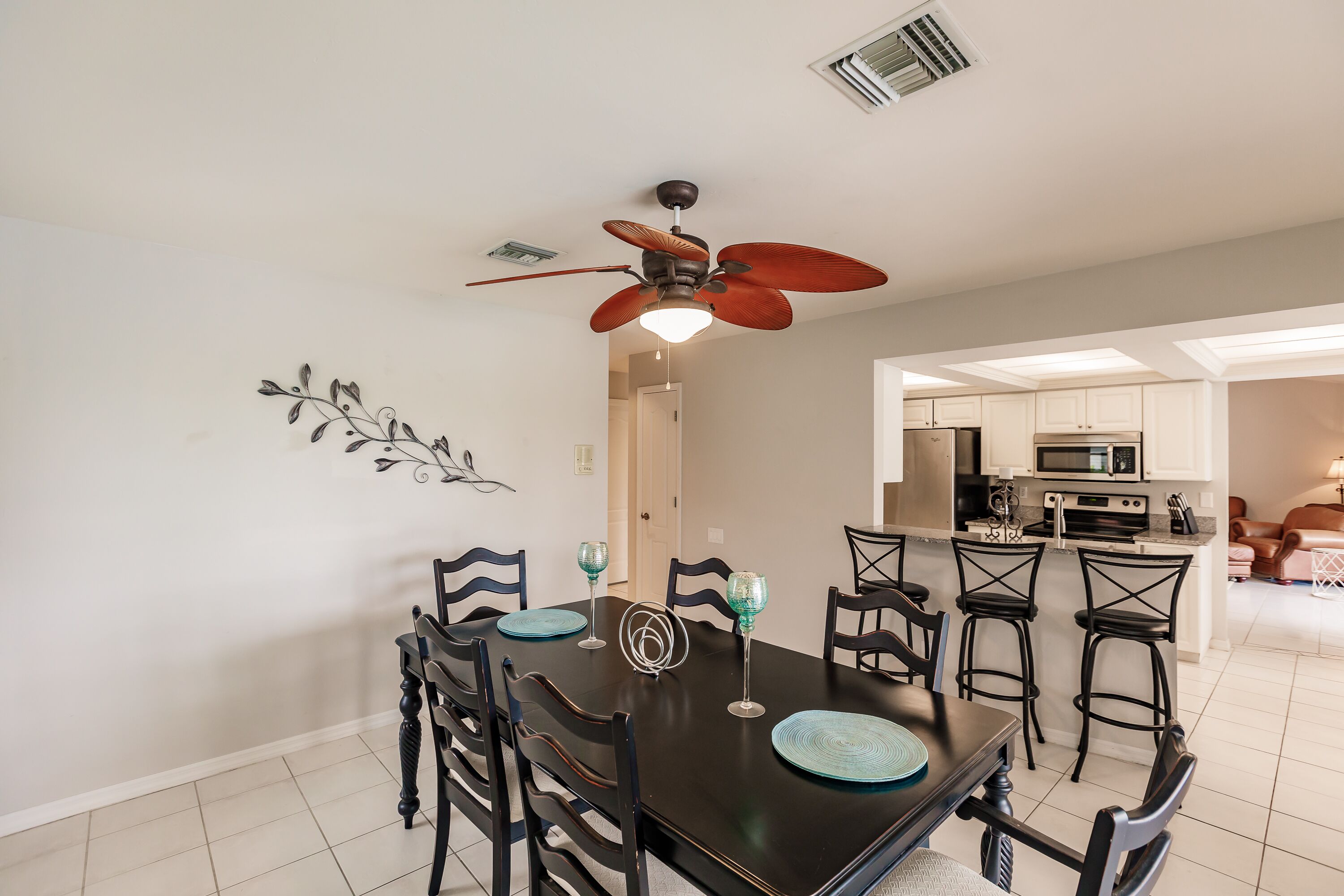 A dining area with a black table, six chairs, and a ceiling fan.