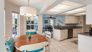 Une cuisine spacieuse avec des meubles blancs, une table à manger en bois et un ventilateur de plafond.