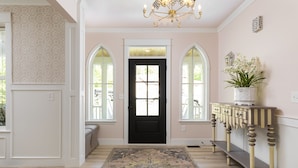 A hallway with a black door, two arched windows, a patterned rug, a console table with a plant, and a chandelier. - Tuck'd Away - Newly Built Vacation Home Located in Downtown Saugatuck (Saugatuck)