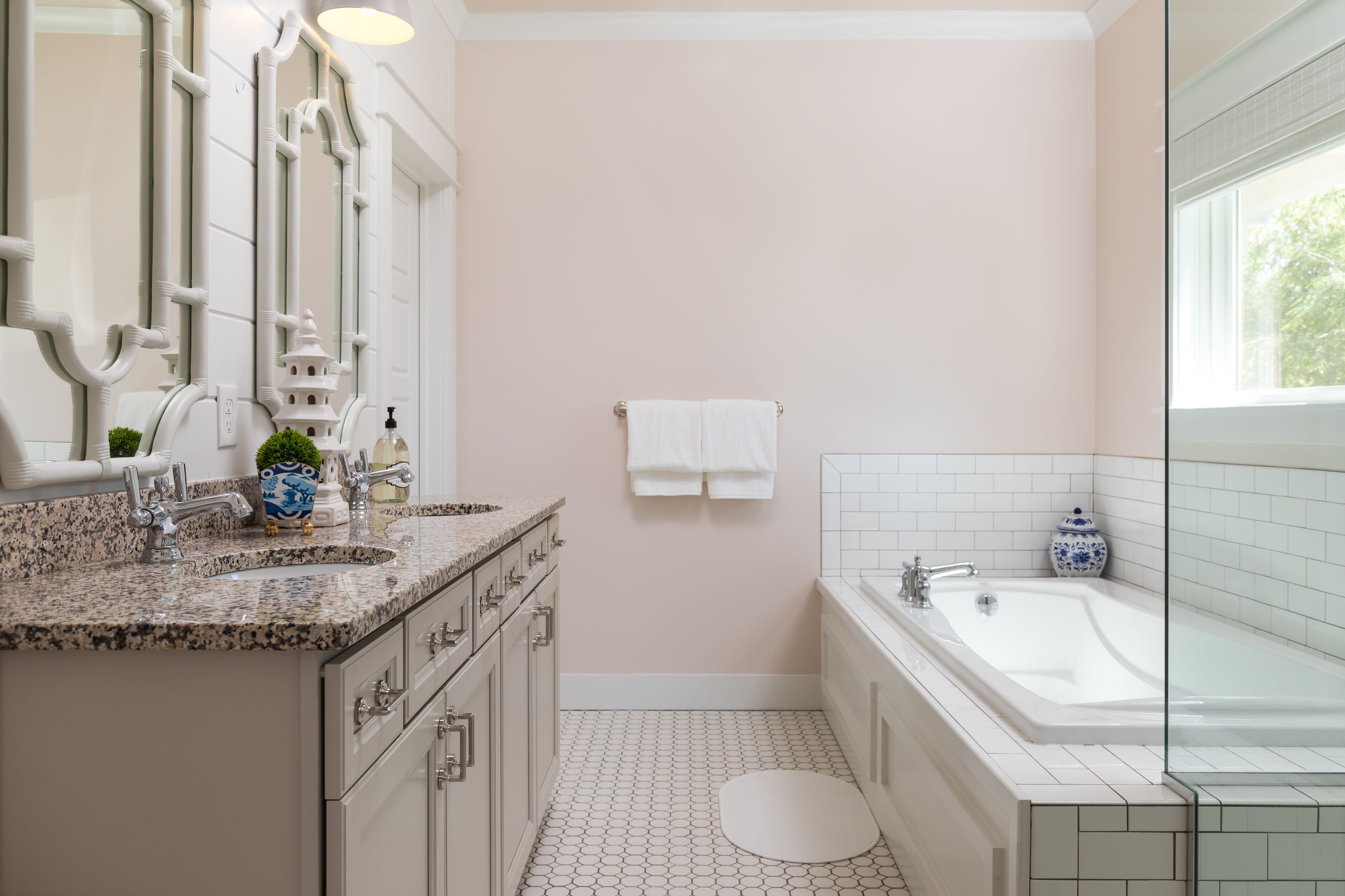 A bathroom with a sink, mirror, and bathtub. There is a towel rack with towels and a small decorative item on the counter.