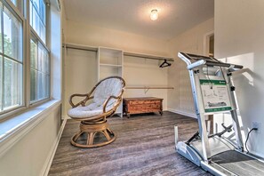 Relax in comfort with a wicker rocking chair near a large window, a wooden chest of drawers for storage, and a treadmill for a workout.