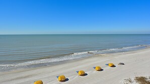 A beach with several yellow beach umbrellas and a clear blue sky.