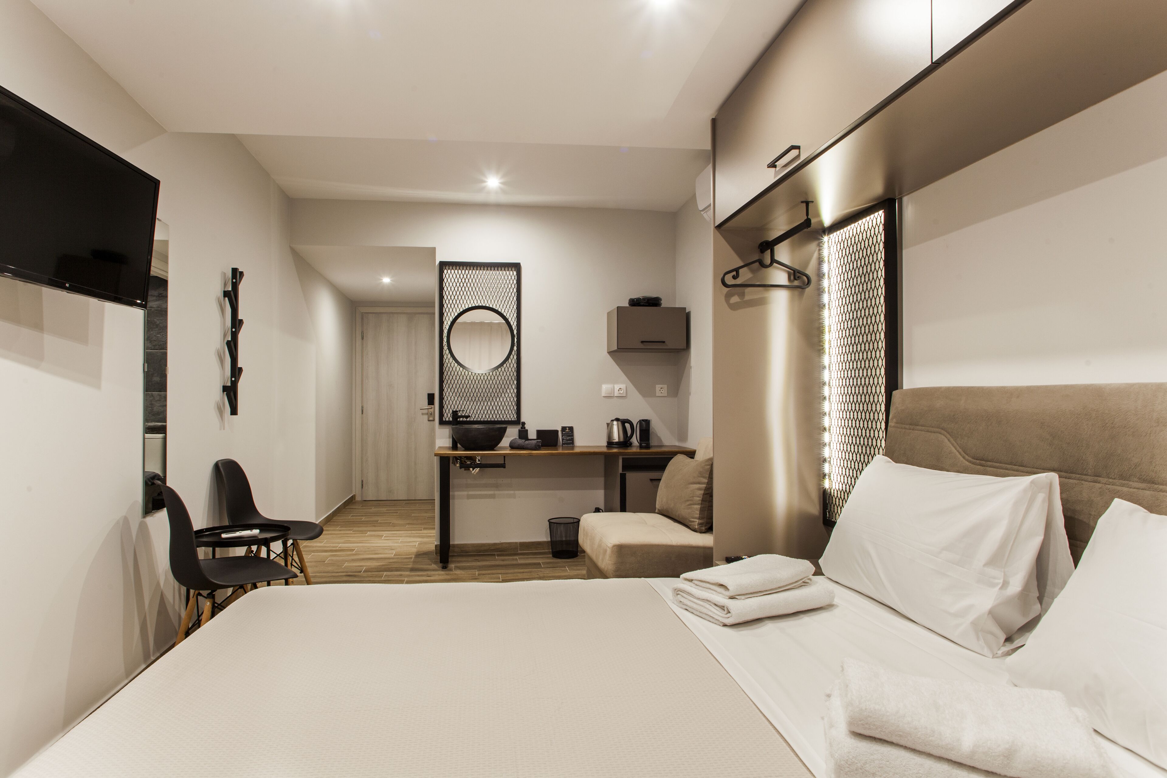 A hotel room with a large bed, a desk with a kettle, a chair, and a TV mounted on the wall.