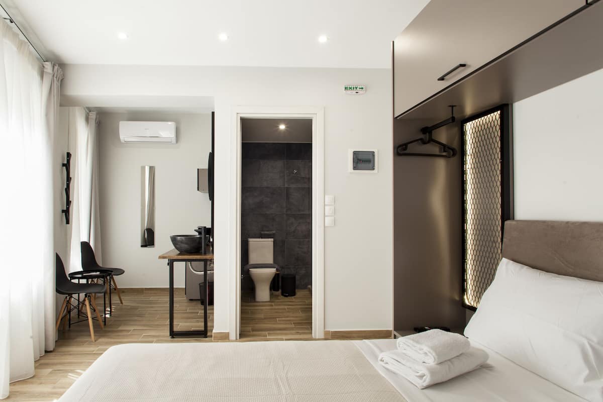 Ein modernes Hotelzimmer mit einem großen Bett, einem Schreibtisch mit Stuhl, einem Badezimmer mit Dusche und einer Klimaanlage an der Wand.