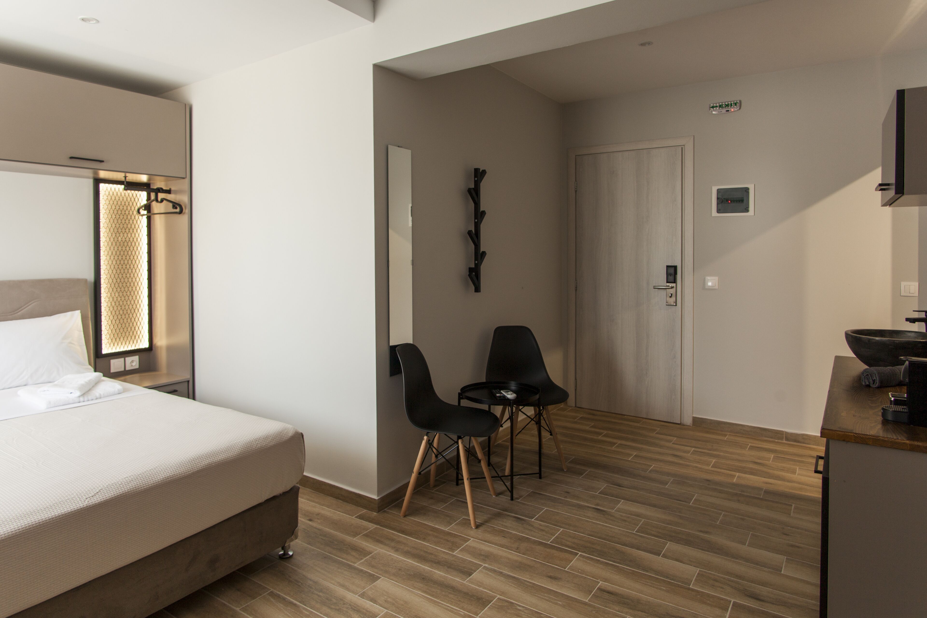 A modern hotel room with a bed, a desk with a sink, and two chairs.