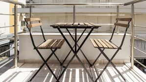 A foldable table with two wooden chairs on a balcony with metal railings. - Raise The Heraklion Project (Heraklion)