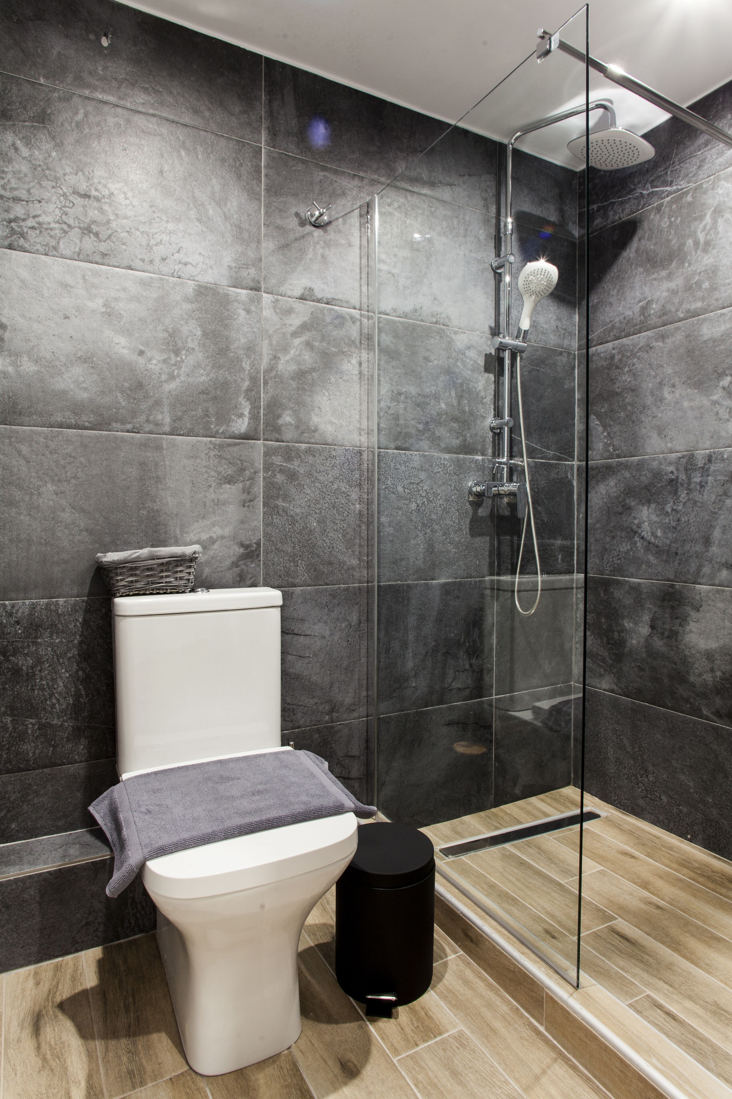 A modern bathroom with a glass-enclosed shower, a white toilet, and a black trash bin.