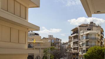 Un edificio de varios pisos con balcones, una calle con coches y peatones, y un cielo despejado.