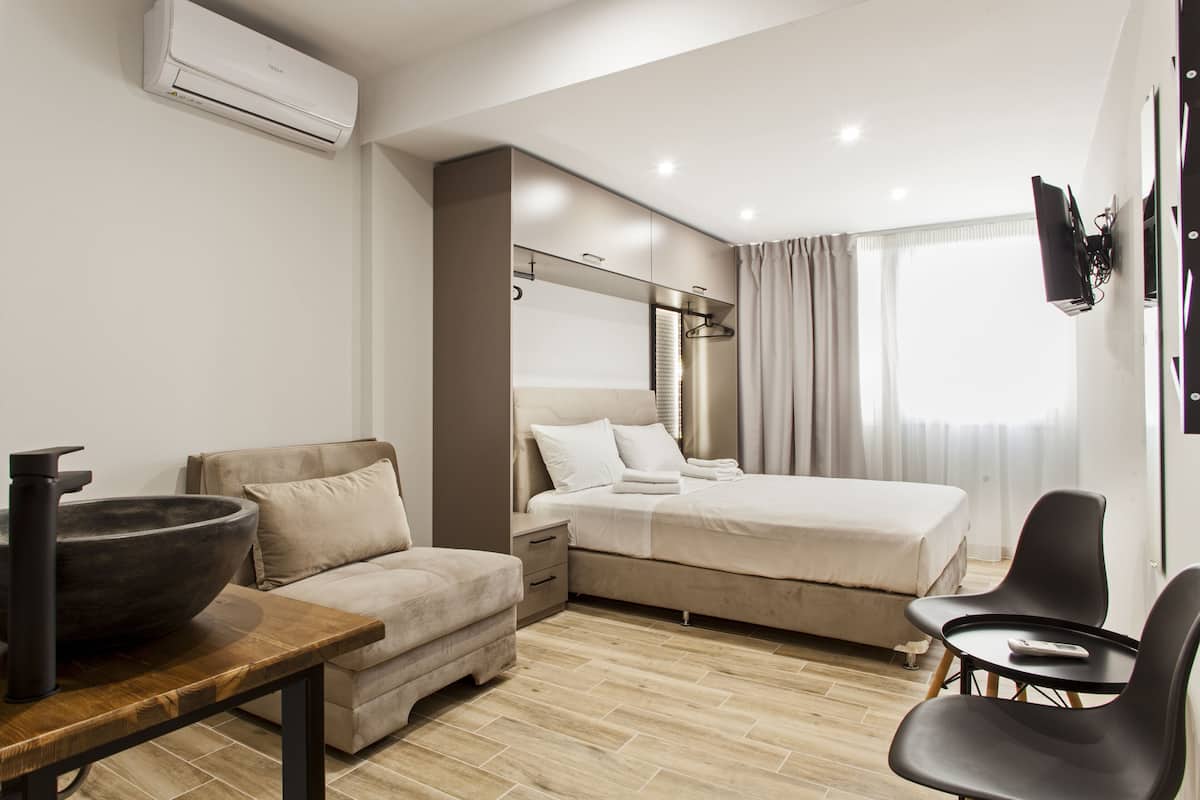 Ein modernes Hotelzimmer mit einem Bett, einer Couch, einem Tisch mit einer Schüssel und einem an der Wand befestigten Fernseher.