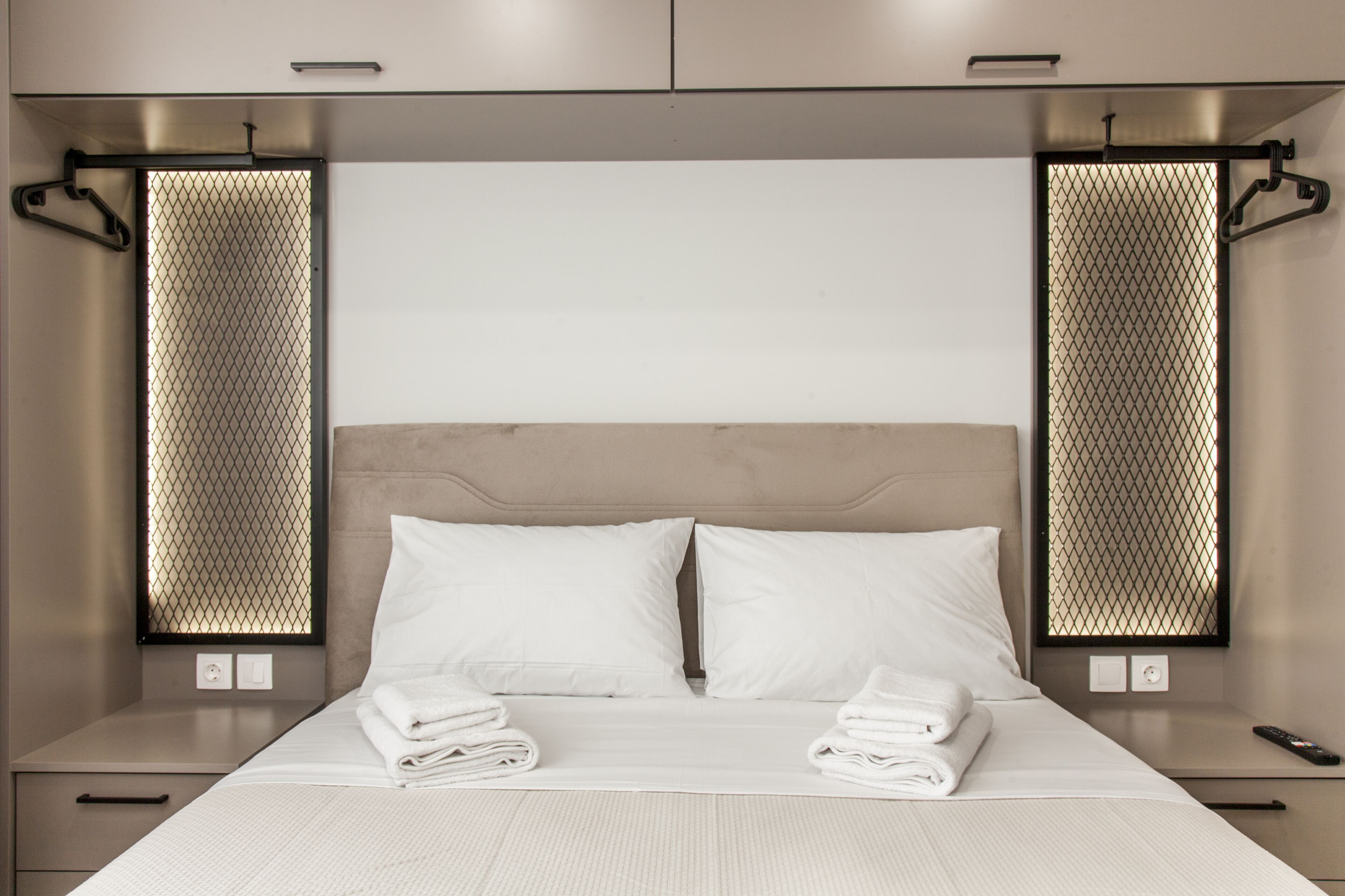 A modern hotel room with a large bed, two bedside tables, and a headboard with a built-in TV.