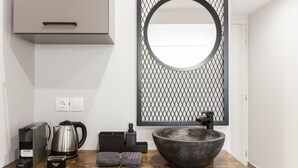 A modern bathroom with a large round mirror, a stone sink, a kettle, a coffee maker, and a towel on a wooden countertop. - Raise The Heraklion Project (Heraklion)