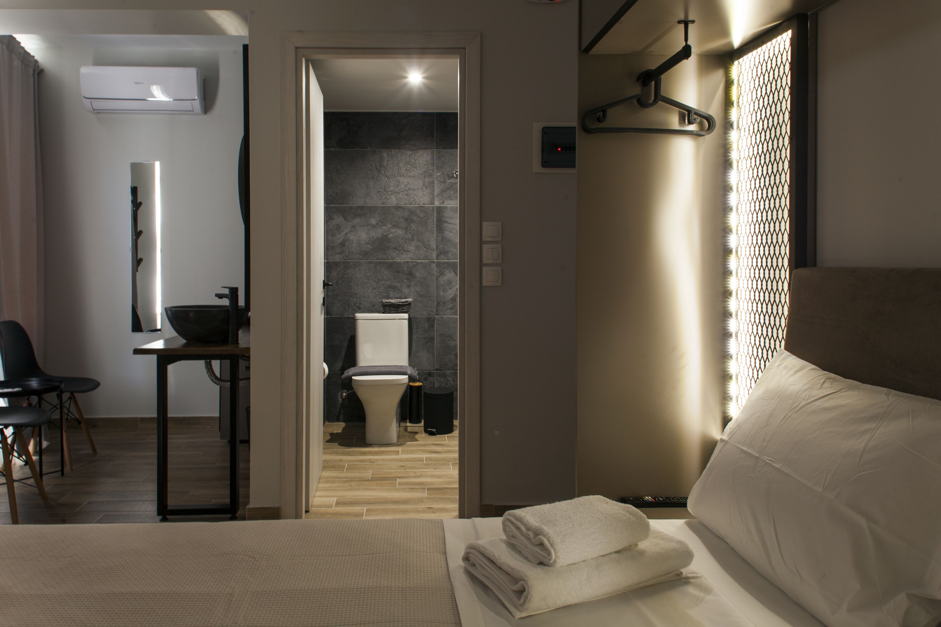 A modern hotel room with a bed, a desk, and a bathroom visible through an open door.
