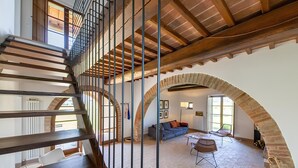 Ein geräumiges Loft mit einer Holztreppe, gewölbten Decken und einem gemütlichen Wohnbereich mit einer Couch und Sesseln.