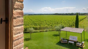 Ein Zimmer mit Steinwand, Blick auf einen Weinberg und Sitzgelegenheit mit Tisch und Stühlen.