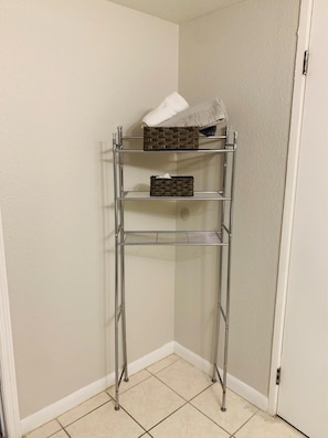 Storage unit with three shelves, each holding a wicker basket, against a wall with a door.