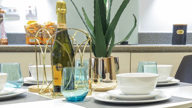 A table set with clear glassware, a bottle of sparkling wine, and a potted plant. - Tudors eSuites Apartment with 4 Beds (Birmingham)
