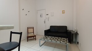 Ein kleiner Wohnbereich mit einer schwarzen Couch, einem Holzstuhl, einem kleinen Tisch und einer weißen Tür mit Schloss.