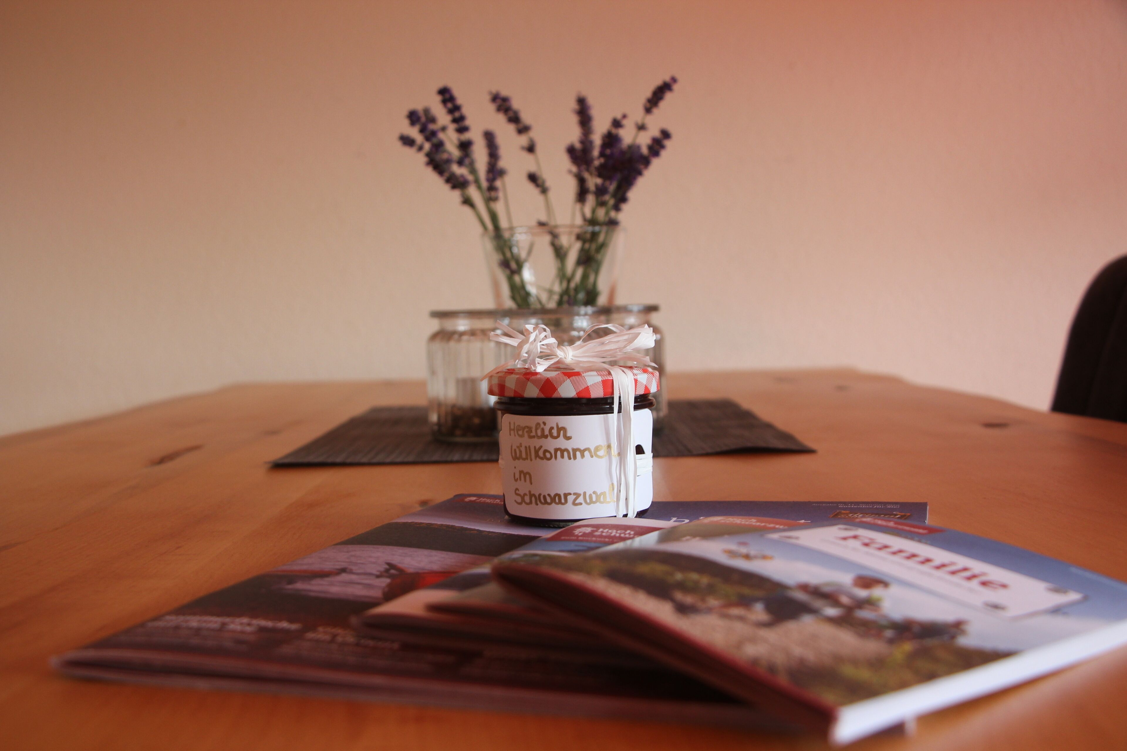 Un tavolo in legno con un barattolo di vetro contenente lavanda, un piccolo contenitore bianco con coperchio rosso e bianco e un libretto intitolato "Familie".