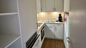 Une cuisine compacte avec des meubles blancs, un plan de travail en bois, un évier et une machine à café.