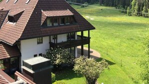 Une maison avec un toit en pente, un balcon et une vue sur un champ verdoyant et une forêt.