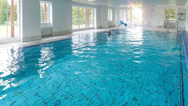 Une piscine intérieure à l’eau claire, dotée de grandes fenêtres et bénéficiant d’un environnement ensoleillé.