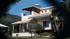 A two-story house with a balcony, a pergola, and a mountain backdrop.