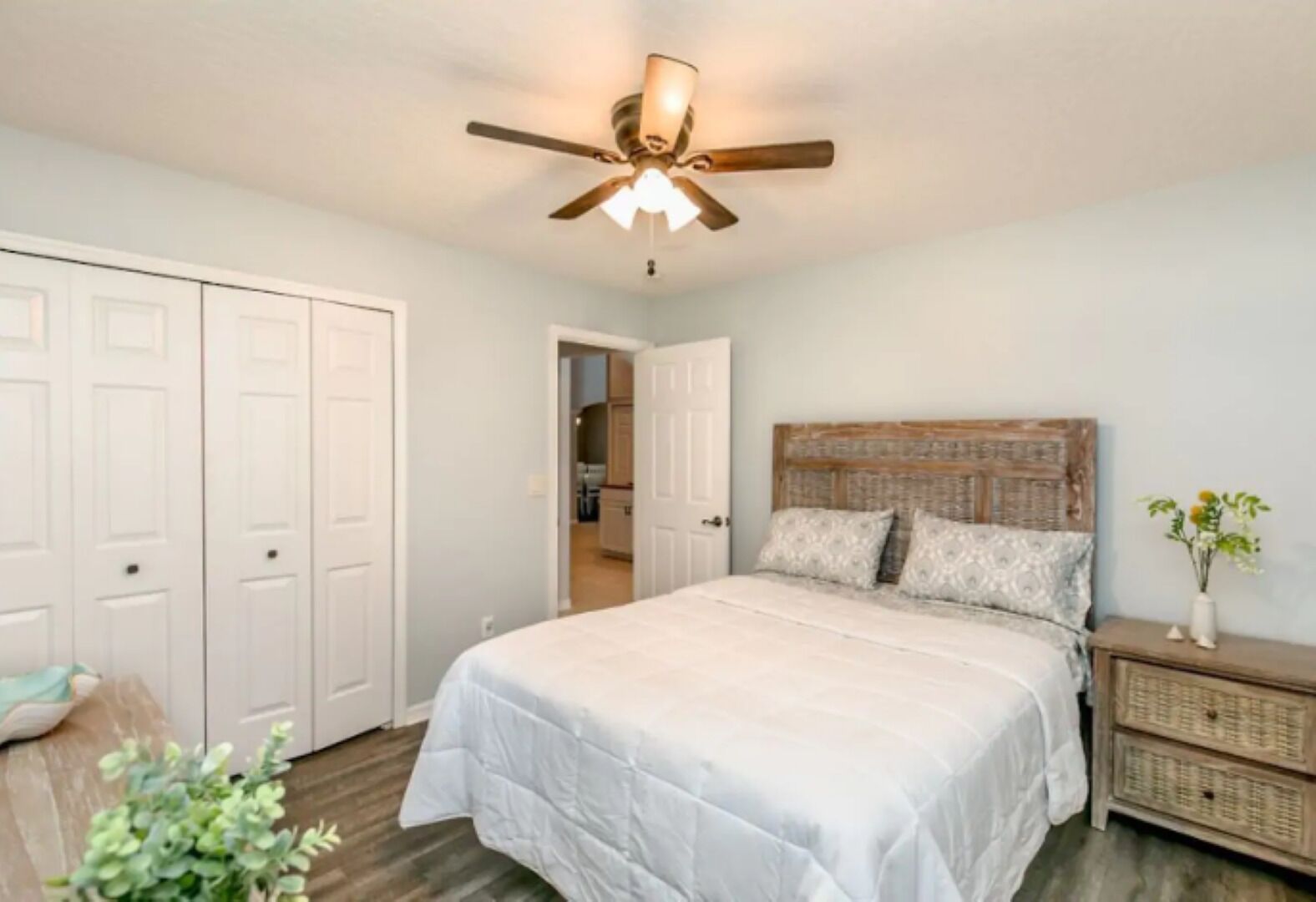A bedroom with a bed, a ceiling fan, a nightstand, and a door leading to another room.