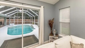 Et værelse med udsigt til et udendørs swimmingpool, en skydedør, en hvid sofa og et lille bord med en vase.