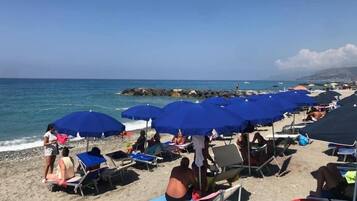 Ein Strand mit Reihen von blauen Sonnenschirmen und Liegestühlen.
