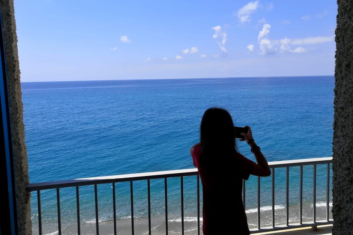 A person taking a photo of the ocean from a balcony with a railing.
