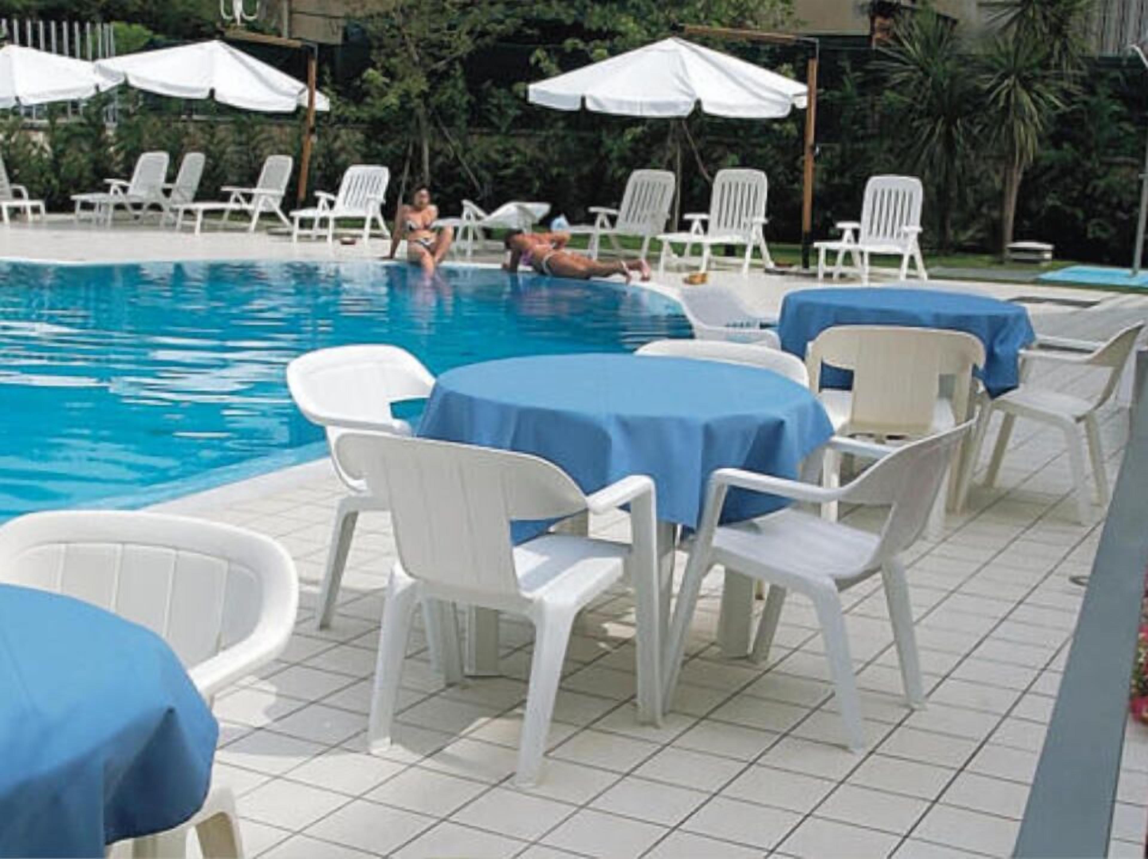 Un espace piscine avec des chaises longues et des tables blanches, dont certaines sont recouvertes de nappes bleues.