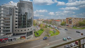 A modern building with a curved glass facade, a parking lot, and a green area with a statue. - Spacious, Comfortable & Purpose-Driven — An Ideal Sofia Stay (Sofia)