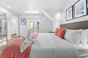 Habitación de hotel moderna con una cama grande, ropa de cama blanca, una manta roja y vistas a la playa a través de la puerta.