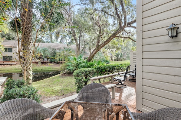 A patio with wicker furniture, a small pond, and a view of a residential area with trees and a building.