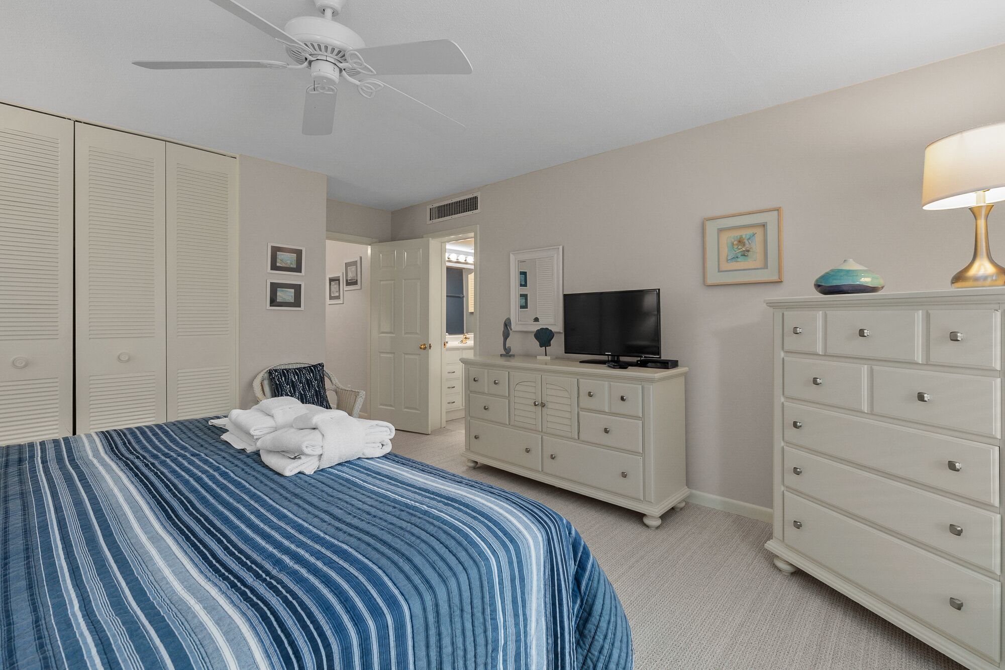 Une chambre à coucher comprenant un lit, une commode, un téléviseur et un ventilateur de plafond.